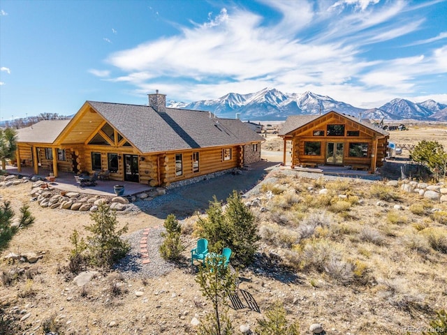 back of house featuring a chimney, french doors, a mountain view, log siding, and a patio