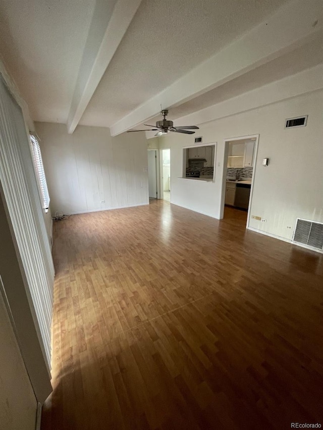 unfurnished living room featuring dark wood-type flooring, ceiling fan, and beamed ceiling