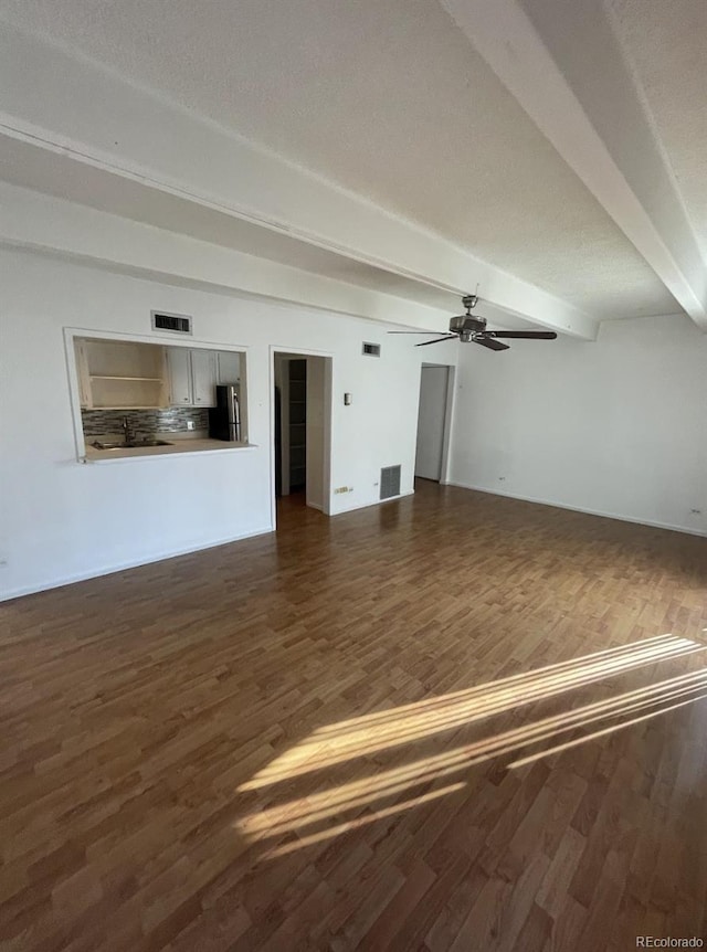 unfurnished living room with dark hardwood / wood-style floors, ceiling fan, and beam ceiling