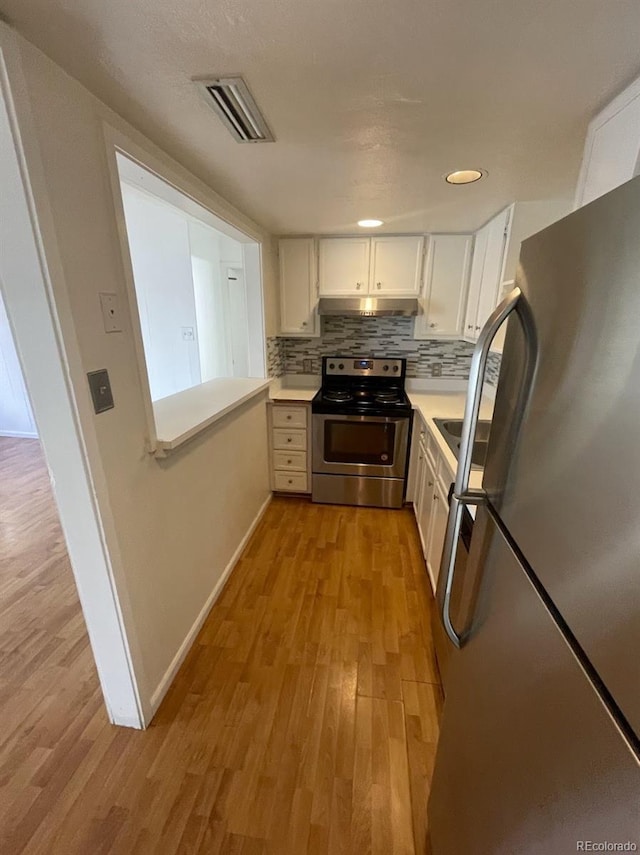 kitchen featuring visible vents, light wood-style flooring, under cabinet range hood, appliances with stainless steel finishes, and backsplash