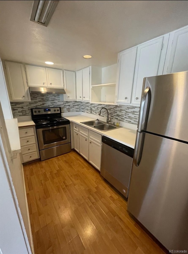 kitchen with a sink, open shelves, under cabinet range hood, wood finished floors, and appliances with stainless steel finishes