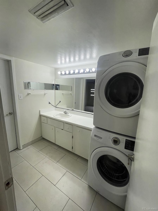 clothes washing area with a sink, visible vents, stacked washer and clothes dryer, and light tile patterned floors