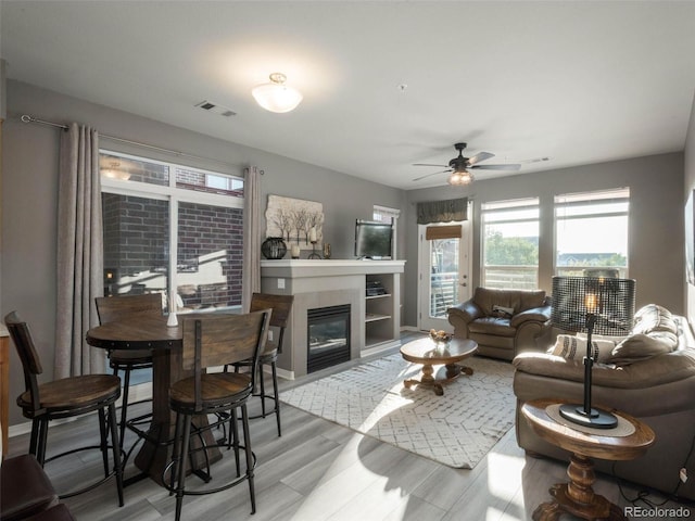 living room with a tile fireplace, light wood-type flooring, and ceiling fan