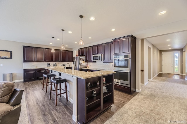 kitchen featuring a large island with sink, dark wood-type flooring, hanging light fixtures, dark brown cabinets, and appliances with stainless steel finishes