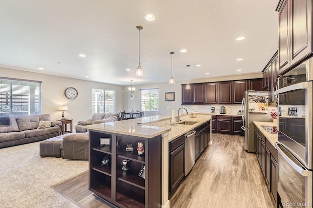 kitchen with dark brown cabinetry, sink, a center island with sink, and hanging light fixtures