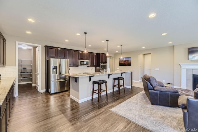 kitchen featuring a tiled fireplace, a kitchen breakfast bar, an island with sink, appliances with stainless steel finishes, and tasteful backsplash