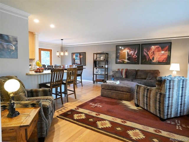 living area featuring light wood finished floors, crown molding, decorative columns, and an inviting chandelier
