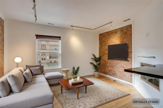 living room with hardwood / wood-style floors, brick wall, and rail lighting