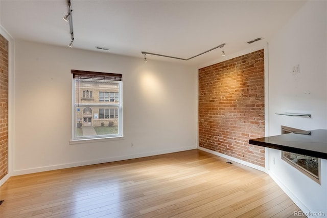 interior space featuring brick wall, light wood-type flooring, visible vents, and track lighting