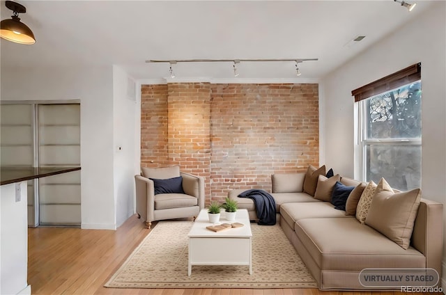 living room featuring light wood-type flooring, brick wall, baseboards, and track lighting