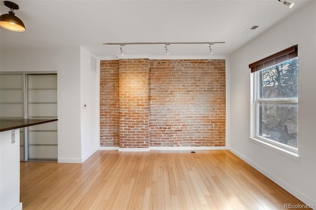 unfurnished dining area featuring baseboards, brick wall, visible vents, and light wood-style floors