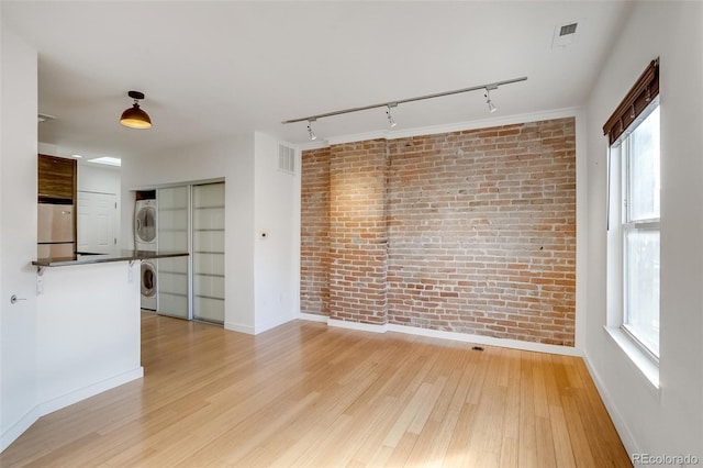 empty room featuring light wood-type flooring, stacked washer / dryer, visible vents, and brick wall