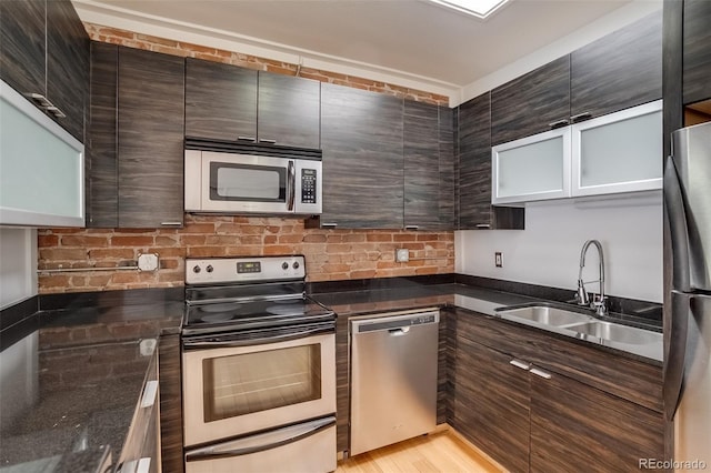 kitchen featuring modern cabinets, appliances with stainless steel finishes, dark stone countertops, dark brown cabinets, and a sink