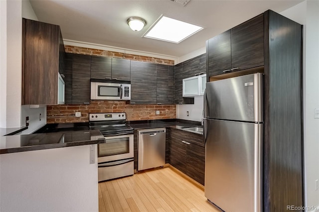 kitchen with dark countertops, modern cabinets, appliances with stainless steel finishes, light wood-type flooring, and a sink