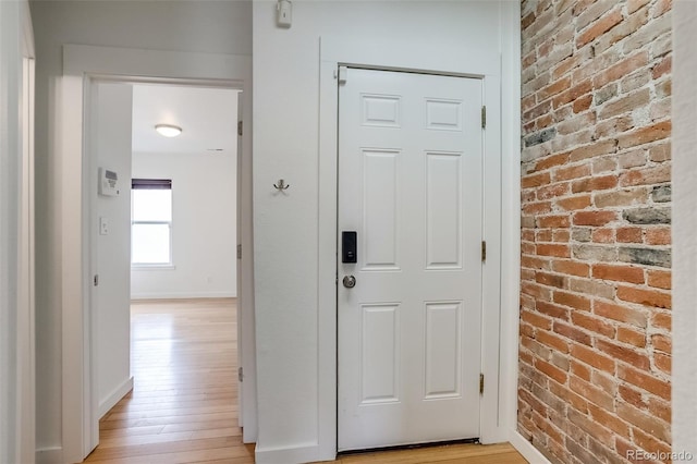 corridor featuring brick wall, light wood finished floors, and baseboards