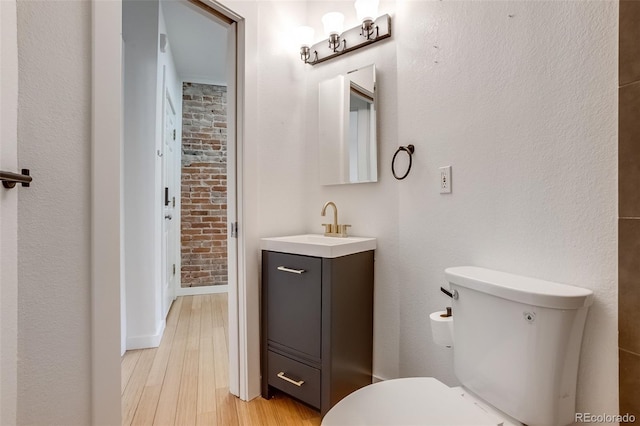 bathroom with brick wall, vanity, toilet, and wood finished floors