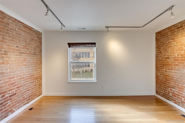 unfurnished room with track lighting, wood-type flooring, and brick wall