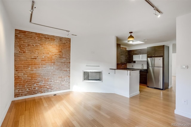 kitchen with dark countertops, light wood finished floors, brick wall, and freestanding refrigerator