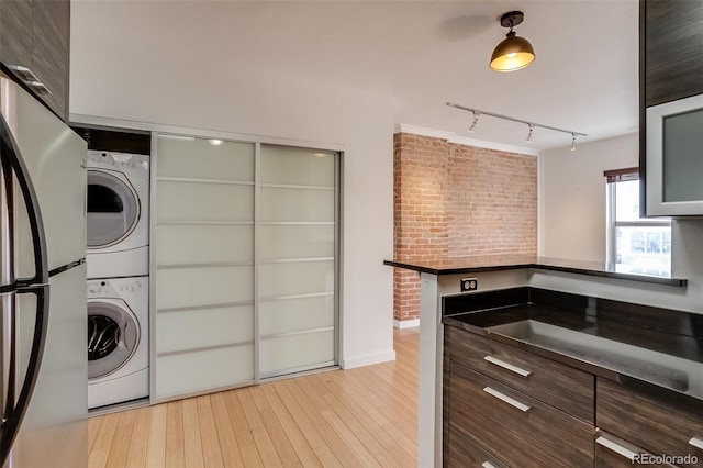 laundry room with light wood finished floors, rail lighting, brick wall, stacked washing maching and dryer, and laundry area