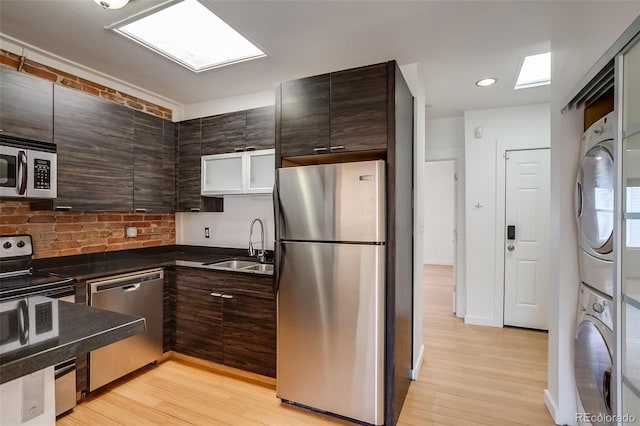 kitchen with dark brown cabinets, appliances with stainless steel finishes, dark countertops, and stacked washer / drying machine