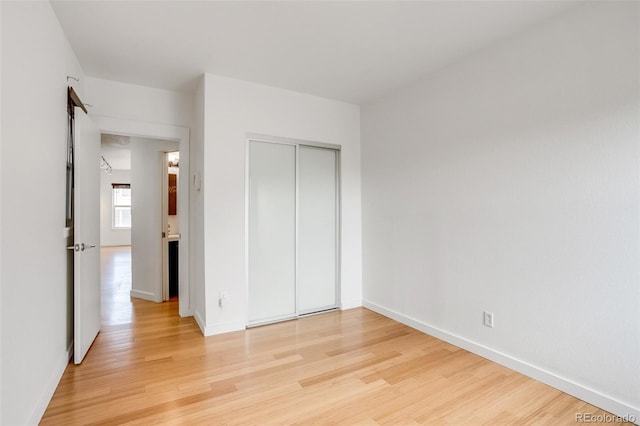 unfurnished bedroom featuring light wood-type flooring, baseboards, and a closet