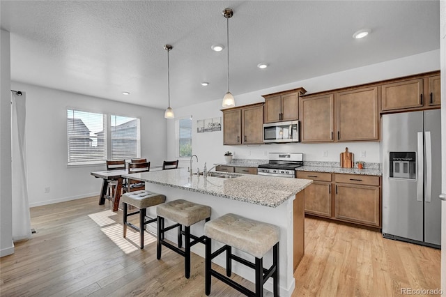 kitchen featuring sink, a breakfast bar, appliances with stainless steel finishes, a kitchen island with sink, and hanging light fixtures