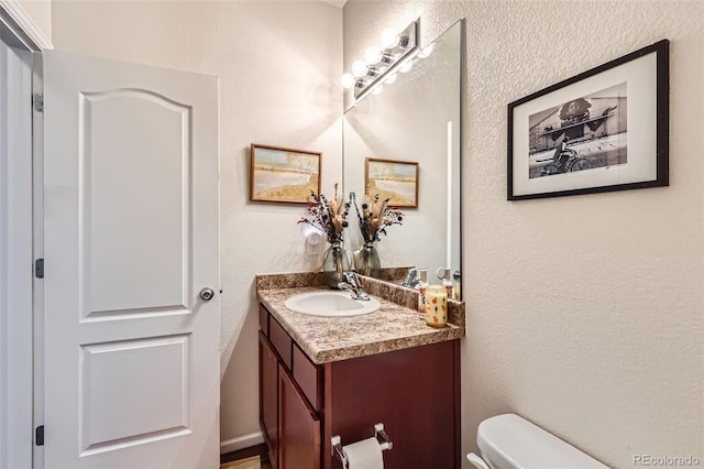 bathroom featuring toilet, vanity, and a textured wall