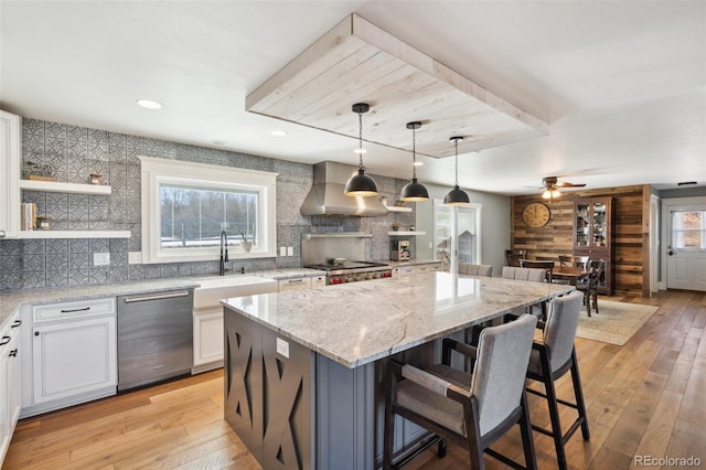 kitchen featuring a center island, stainless steel appliances, light wood-style flooring, a sink, and wall chimney range hood