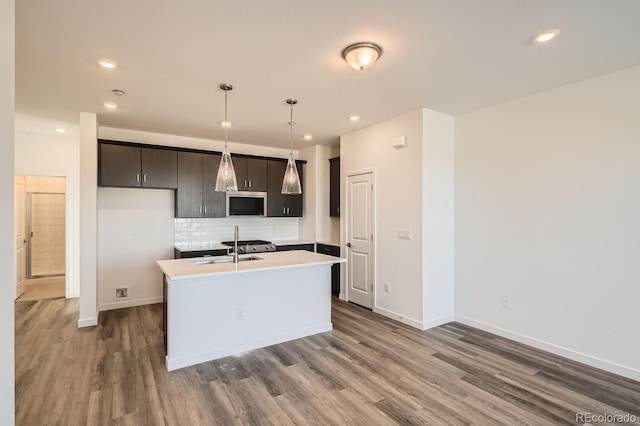 kitchen with sink, tasteful backsplash, dark hardwood / wood-style floors, an island with sink, and decorative light fixtures