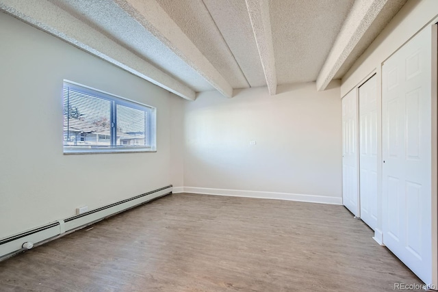 unfurnished bedroom with a textured ceiling, beamed ceiling, a baseboard radiator, and wood finished floors