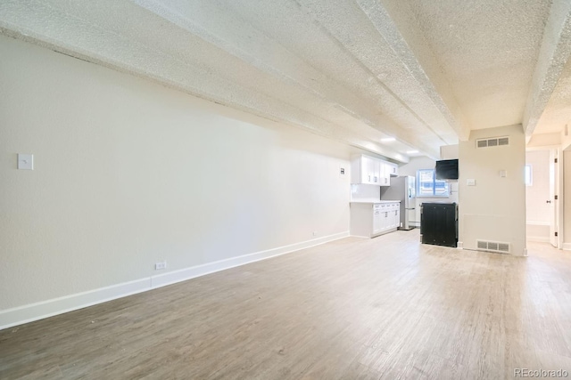 unfurnished living room featuring baseboards, a textured ceiling, visible vents, and wood finished floors