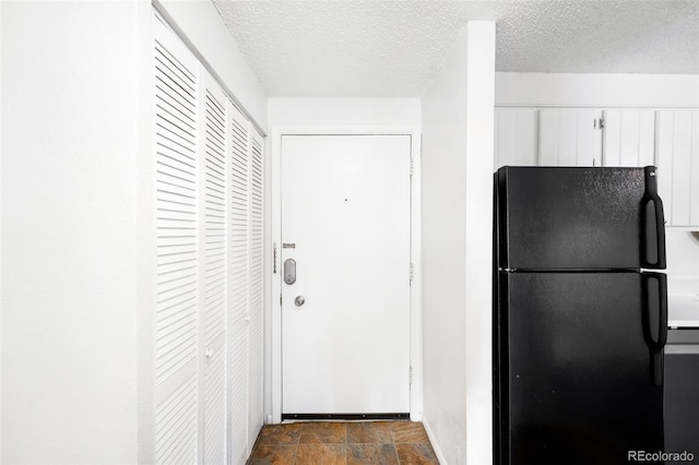 kitchen with white cabinets, a textured ceiling, and black refrigerator