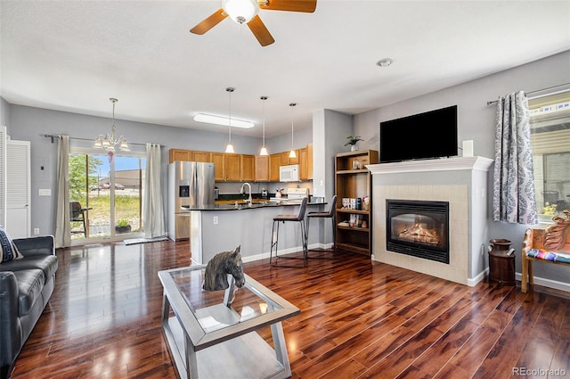 living room featuring a fireplace, ceiling fan with notable chandelier, dark wood-type flooring, and sink