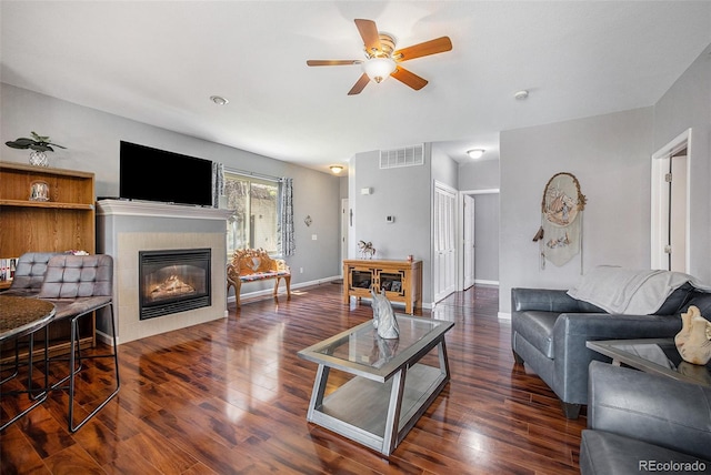 living room featuring a tiled fireplace, ceiling fan, and dark wood-type flooring