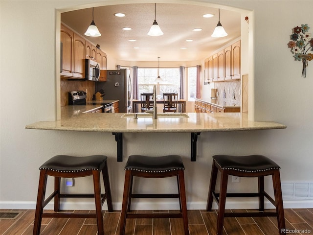 kitchen with a kitchen bar, appliances with stainless steel finishes, sink, pendant lighting, and tasteful backsplash