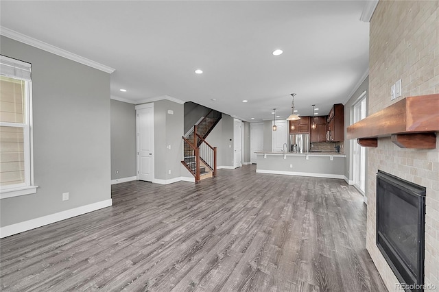 unfurnished living room with dark wood-type flooring, ornamental molding, a brick fireplace, baseboards, and stairs