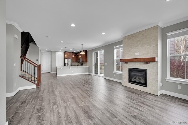 unfurnished living room featuring dark wood-style floors, a fireplace, stairway, ornamental molding, and baseboards