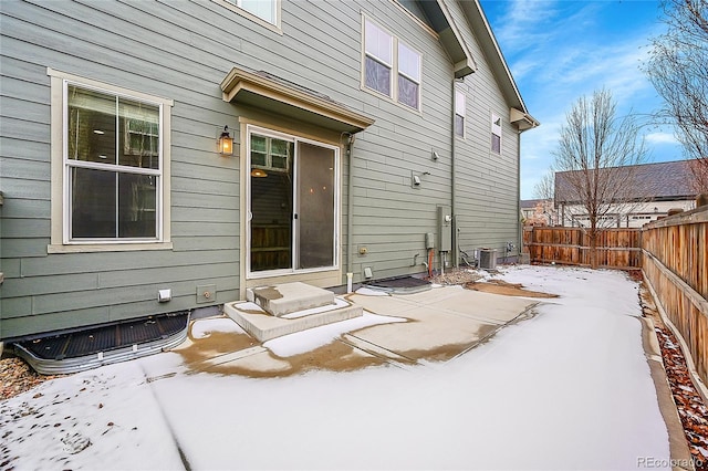 snow covered rear of property with entry steps, a fenced backyard, a patio area, and cooling unit