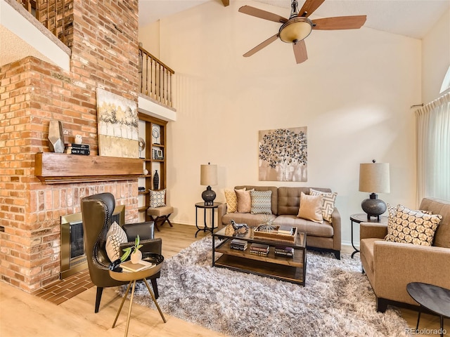 living room with hardwood / wood-style flooring, ceiling fan, high vaulted ceiling, a brick fireplace, and beamed ceiling