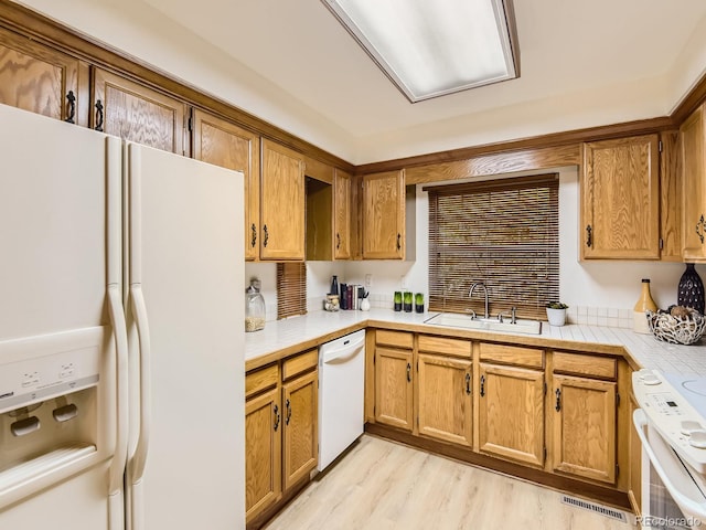 kitchen with sink, white appliances, tile countertops, and light wood-type flooring