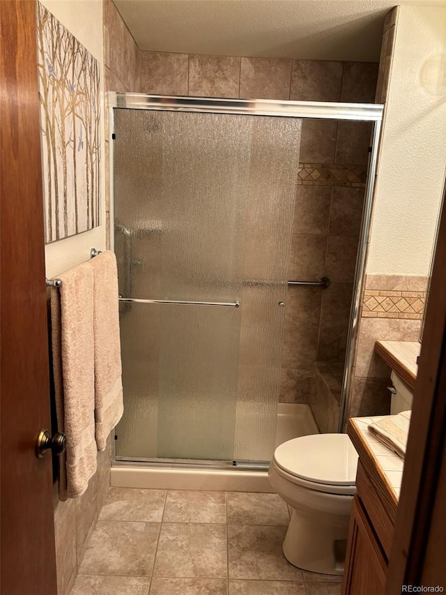 bathroom with a shower with shower door, tile walls, tile patterned flooring, vanity, and toilet