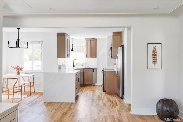 kitchen featuring appliances with stainless steel finishes, sink, hanging light fixtures, light stone counters, and light wood-type flooring