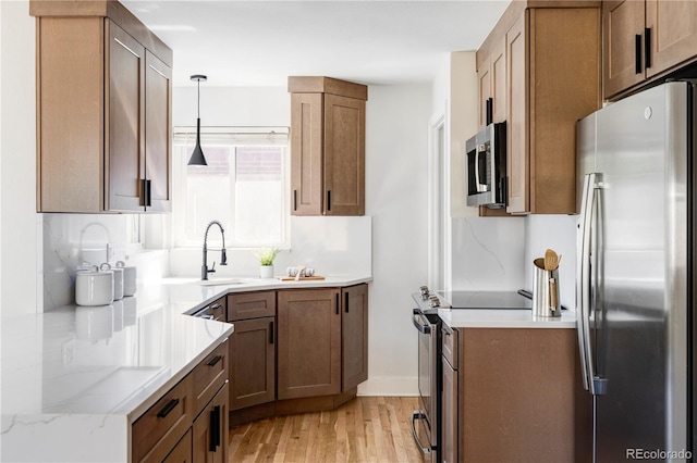 kitchen with sink, light stone counters, hanging light fixtures, light wood-type flooring, and stainless steel appliances