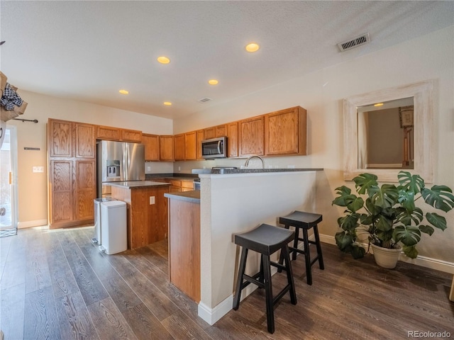 kitchen featuring dark hardwood / wood-style floors, appliances with stainless steel finishes, a kitchen island, kitchen peninsula, and a breakfast bar area