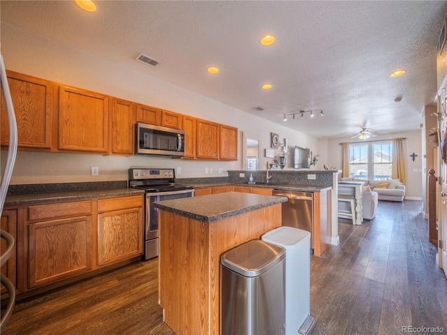 kitchen with a textured ceiling, appliances with stainless steel finishes, a center island, dark hardwood / wood-style flooring, and sink