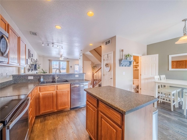 kitchen featuring appliances with stainless steel finishes, sink, hardwood / wood-style floors, a textured ceiling, and a kitchen island