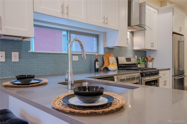 kitchen with decorative backsplash, wall chimney range hood, white cabinetry, and stainless steel appliances