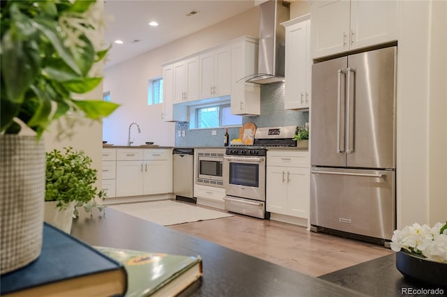 kitchen with sink, white cabinetry, light hardwood / wood-style flooring, stainless steel appliances, and wall chimney exhaust hood