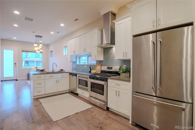 kitchen featuring kitchen peninsula, appliances with stainless steel finishes, decorative light fixtures, wall chimney exhaust hood, and sink