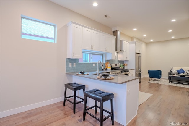 kitchen with kitchen peninsula, white cabinetry, stainless steel appliances, and wall chimney exhaust hood